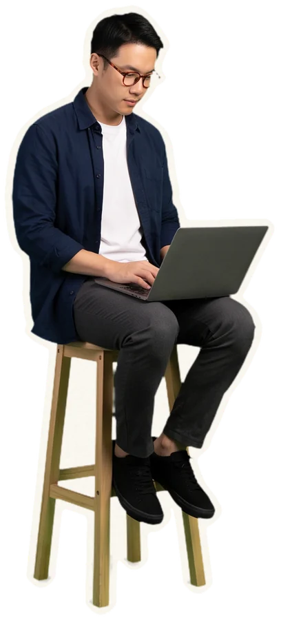 A filmmaker sits on a stool, working on a laptop