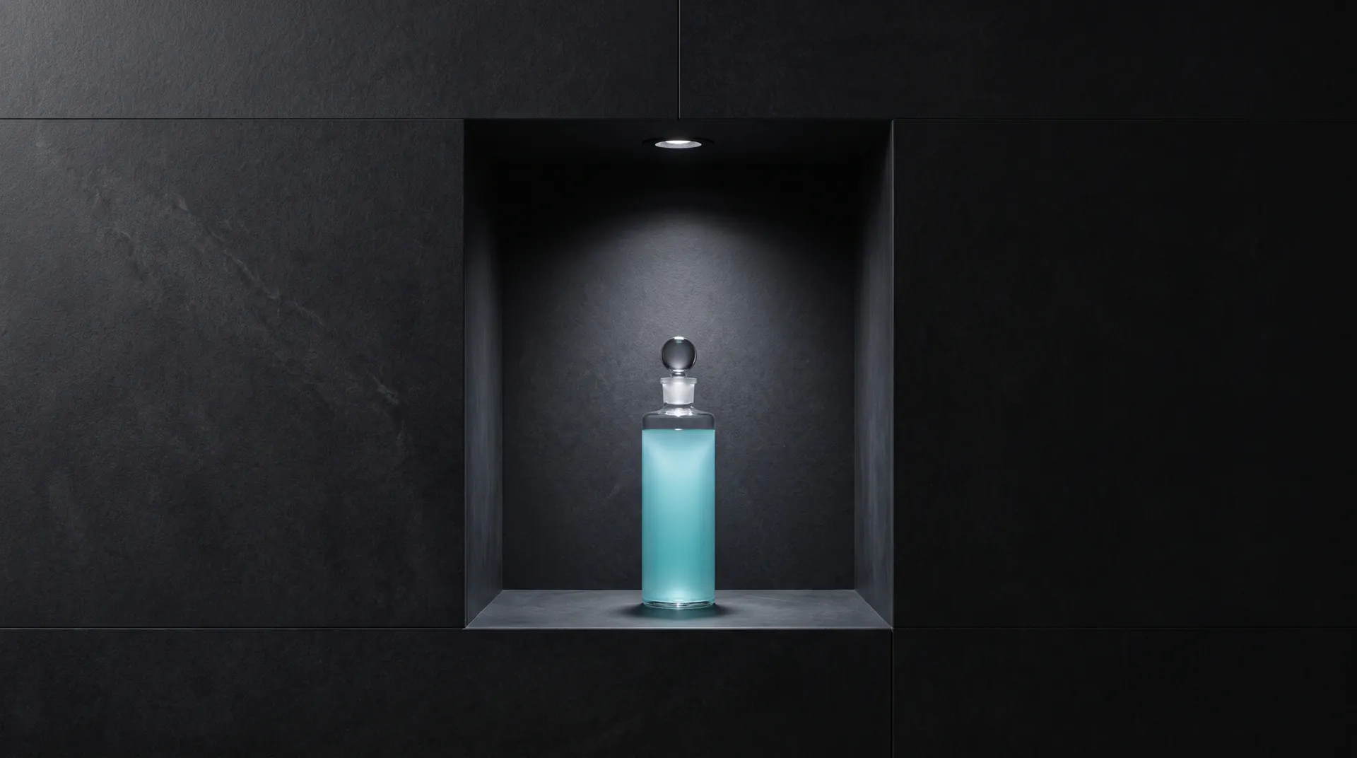 A glass bottle of pale blue liquid alone in a dark stone niche, lit from above